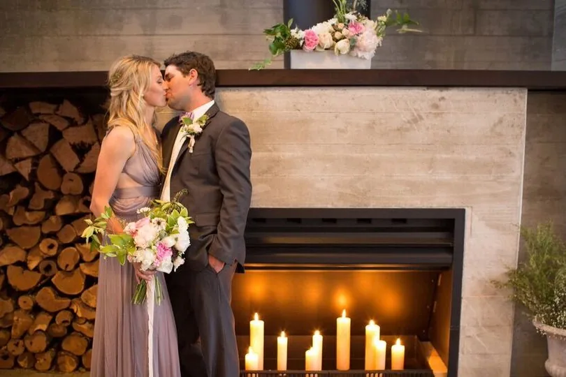 Couple kissing by a candlelit fireplace with stacked firewood beside them