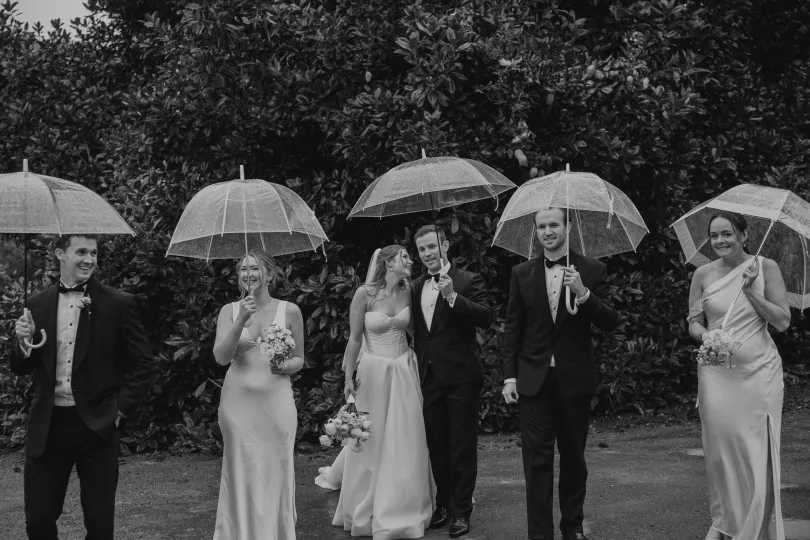 Wedding party in formalwear holding clear umbrellas, smiling in soft winter light